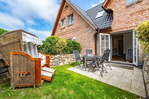Et murstenshus med terrasse, en fletstol og et bord.