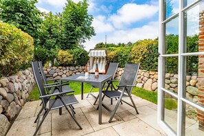 En udendørs terrasse med stenvæg, et bord med stole og en grill.