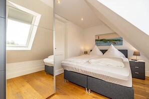 A bedroom with a skylight, a bed with white linens, a nightstand with a lamp, and a painting on the wall.