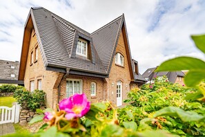 Ein zweistöckiges Haus mit steilem Dach, Ziegelaußenwand und einer kleinen Veranda.