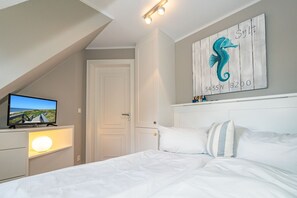 Ein Schlafzimmer mit Bett, Fernseher auf einem Nachttisch, einer Tür und einem Seepferd-Kunstwerk an der Wand.