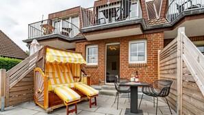 Une terrasse avec une chaise longue à rayures, une table avec des chaises et une bouteille de vin.