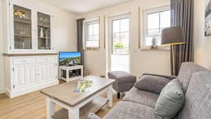 Un salon comprenant un canapé, une table basse, un téléviseur et un meuble avec des portes en verre.
