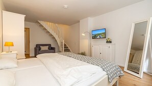Une chambre à coucher comprenant un lit, une chaise, un bureau avec une lampe, une télévision, une armoire et un miroir.