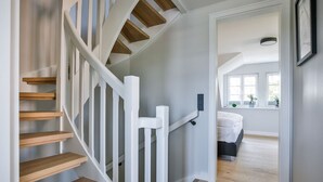 A staircase with wooden steps and white railings leading to a bedroom with a bed and a window.