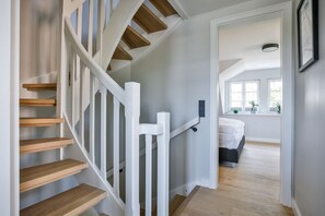 A staircase with wooden steps and white railings leading to a bedroom with a bed and a window.