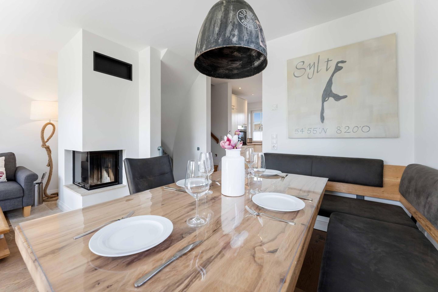 Een moderne eetruimte met een houten tafel voor vier personen, een open haard en een kunstwerk aan de muur.
