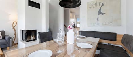 A modern dining room with a wooden table set for four, a fireplace, and a wall-mounted artwork.