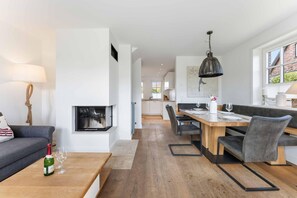 Un salon moderne avec une cheminée, un coin repas avec une table et des chaises en bois, et une cuisine en arrière-plan.