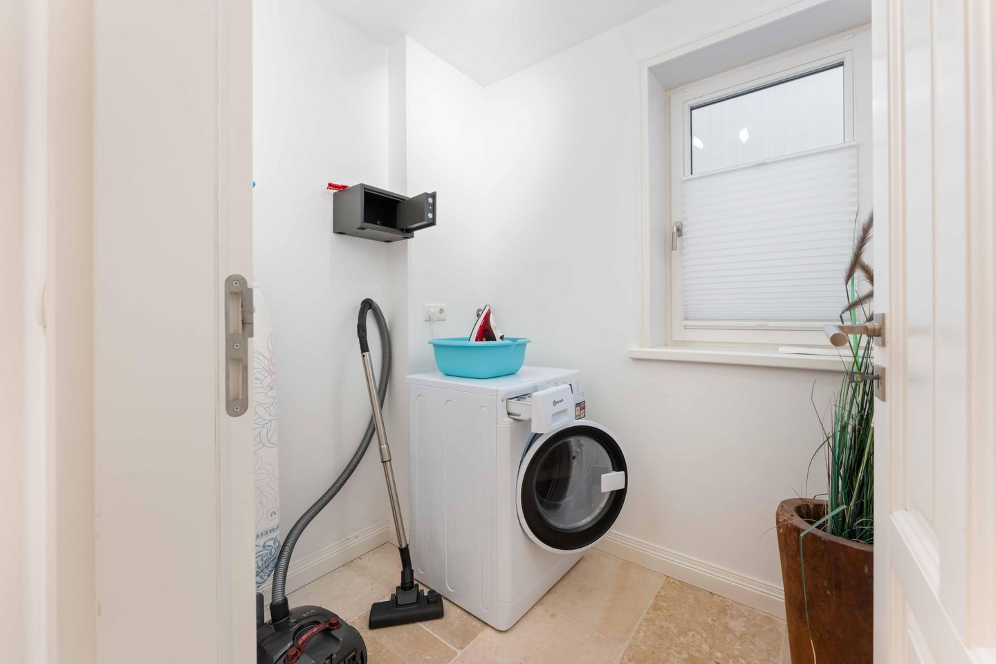 Een praktische wasruimte met een wasmachine, stofzuiger en een klein raam.