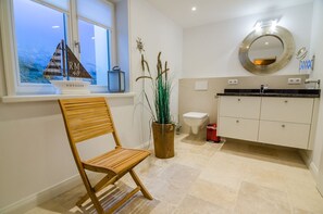 Un baño moderno con una silla de madera, una planta en maceta, un inodoro y un mueble de tocador con espejo.