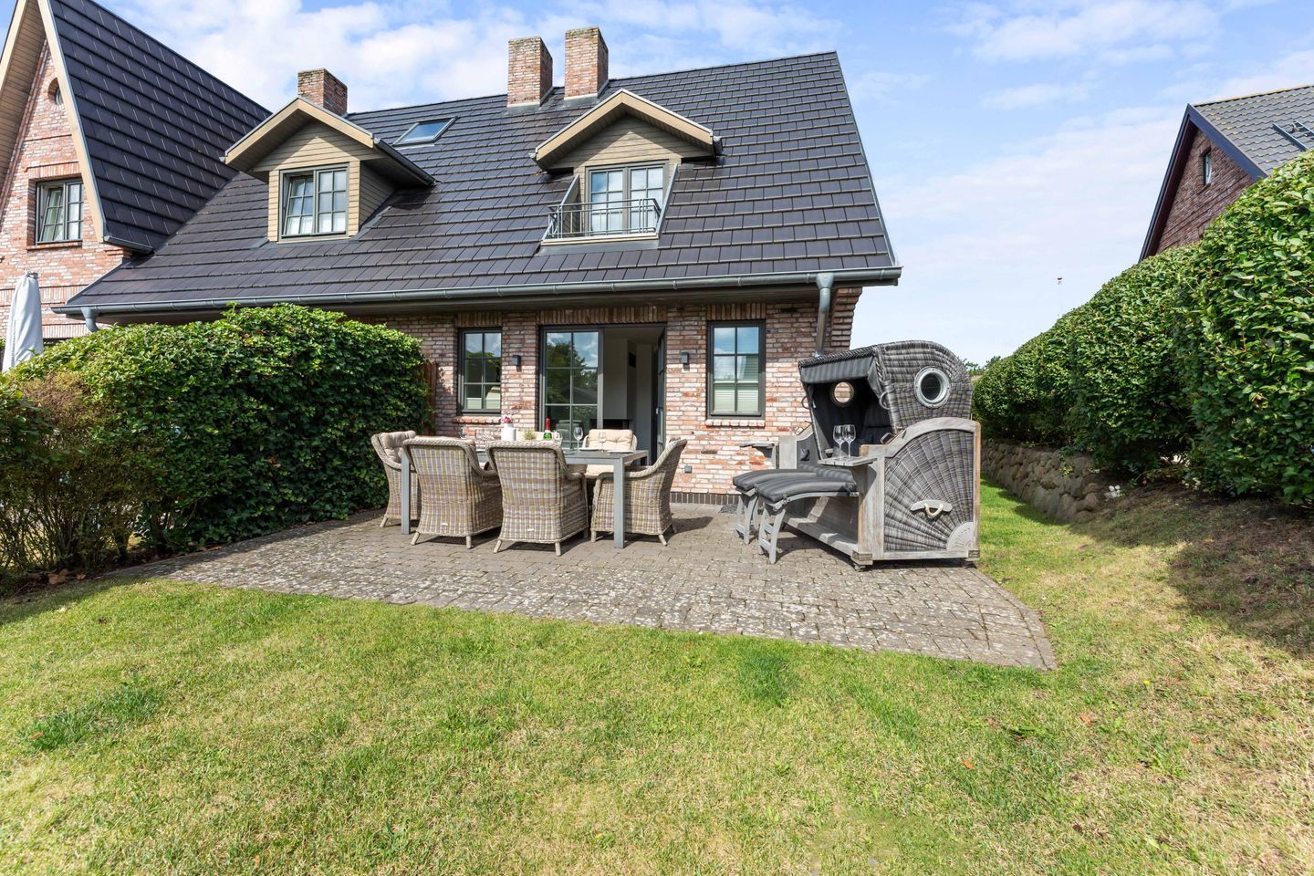 Ein Haus mit Ziegelaußenwand, einem dunklen Schindeldach und einer gepflasterten Terrasse mit Gartenmöbeln.