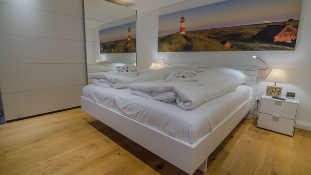 Un dormitorio moderno con una cama grande, una mesita de noche, un espejo y dos cuadros de faros.