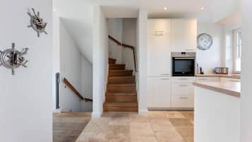A modern kitchen with a built-in oven, a clock, and a wooden staircase leading to another room.