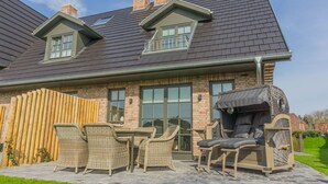 Una casa con patio, amueblado con mobiliario de mimbre y una parrilla cubierta.