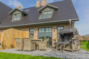 A house with a patio area featuring wicker furniture and a covered grill.