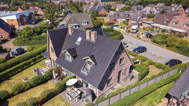 Une grande maison à deux étages, dotée d’un toit en pente, entourée de jardins bien entretenus et d’une cour clôturée.