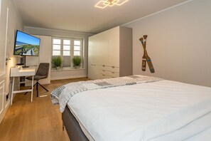 A bedroom with a bed, a desk, a chair, a TV, and a window with plants. - Sylt Oase - Semi-detached vacation home for up to 6 people with a sauna, garden, and (Sylt)