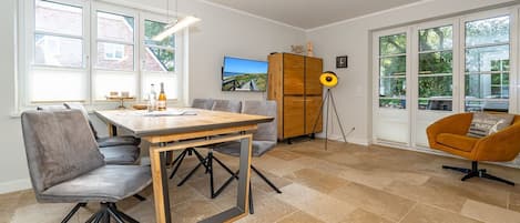 Una zona de menjador moderna amb una taula i cadires de fusta, una televisió i un gran finestral amb vistes.