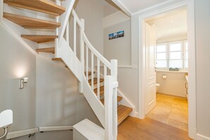 A staircase with wooden steps and white railings leading to a bathroom with a toilet and a window.