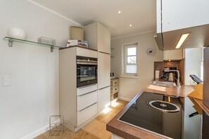 A compact kitchen with a built-in oven, a stovetop, and a window providing natural light. - Sylt Oase - Semi-detached vacation home for up to 6 people with a sauna, garden, and (Sylt)