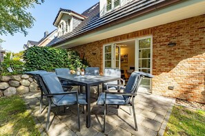 A patio with a table and chairs, a brick wall, and a glass door leading to an interior space.