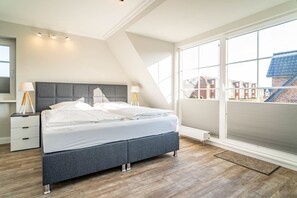 Un dormitorio moderno con una cama grande, una mesita de noche, una lámpara y vistas al exterior a través de amplias ventanas.