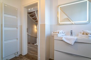 A modern bathroom with a white vanity, a mirror with integrated lighting, and a towel rack.