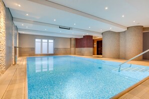 Una piscina interior con agua cristalina, rodeada por paredes con textura similar a la piedra en un lado y paredes lisas en el otro.