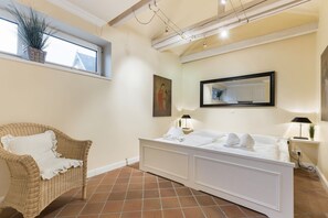 Una habitación de hotel con una silla de mimbre, un tocador blanco, un espejo grande y piso de baldosas.