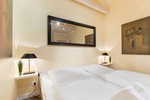 Une chambre d’hôtel avec un grand lit, deux tables de chevet avec des lampes, un miroir fixé au mur et un tableau.