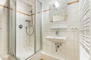 Un baño moderno con ducha envuelta en vidrio, un lavamanos blanco con espejo arriba y un perchero a la derecha.