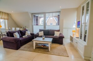 Un salon avec deux canapés, une table basse et une grande fenêtre donnant sur des immeubles.