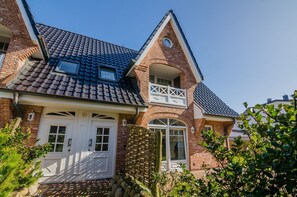 Une maison à deux étages avec une façade en briques, un toit en tuiles et un petit balcon doté de balustrades blanches.