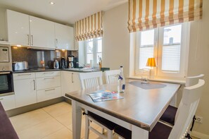 A modern kitchen with white cabinets, a built-in oven, a coffee maker, and a dining table with chairs.