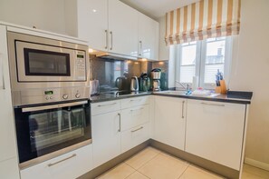 A modern kitchen with stainless steel appliances, white cabinetry, and a striped window valance.