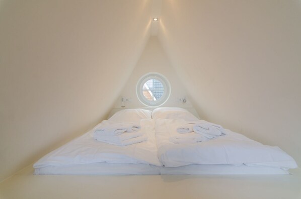 A triangular room with a bed centered under a circular skylight.