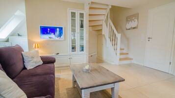 Ein Wohnzimmer mit Sofa, Couchtisch, Fernseher, Schrank und Treppe.