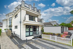 A two-story house with a balcony, a white picket fence, and a paved driveway. - Wattmuschel - vacation apartment for up to 4 people with terrace and sauna. (Sylt)