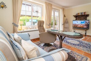 Un salon chaleureux avec un canapé, une table basse en verre, un fauteuil et un téléviseur posé sur un meuble en bois.