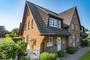 A two-story brick house with a steeply pitched roof, a front porch, and a gated entrance. - Kate Kleinod - Neu!!! Ab September 2022 in der Vermittlung. - Schönes Reihenendhaus in Ruhiger Lage (Sylt-Ost)