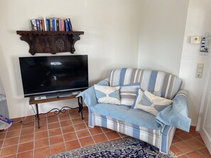 A living room with a flat-screen TV, a striped sofa, a patterned rug, and a wooden shelf with books.