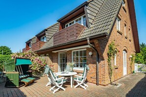 A two-story house with a brick exterior, a tiled roof, and a patio with outdoor furniture. - Kate Kleinod - Neu!!! Ab September 2022 in der Vermittlung. - Schönes Reihenendhaus in Ruhiger Lage (Sylt-Ost)
