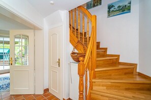 A wooden staircase with a basket hanging from the balustrade, white doors, and a view of the outside. - Kate Kleinod - Neu!!! Ab September 2022 in der Vermittlung. - Schönes Reihenendhaus in Ruhiger Lage (Sylt-Ost)