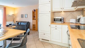 A compact kitchen with white cabinetry, a microwave, toaster, kettle, and a dining area with a table and chairs. - Ammerland Whg. 2 - Spacious 3-room apartment for up to 4 persons, with balcony. (Sylt)