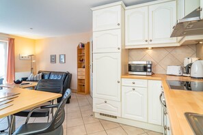 A compact kitchen with white cabinetry, a microwave, toaster, kettle, and a dining area with a table and chairs. - Ammerland Whg. 2 - Spacious 3-room apartment for up to 4 persons, with balcony. (Sylt)