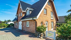 Une maison à deux étages, construite en briques, avec un toit à forte pente, des fondations en pierre et une clôture blanche en bois.