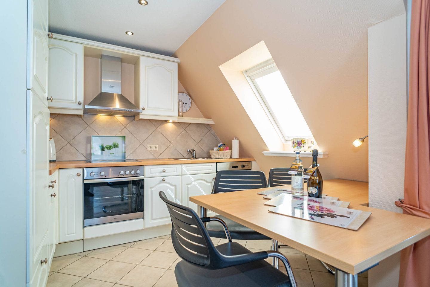 A compact kitchen with white cabinets, a built-in oven, a dining table with four chairs, and a skylight.