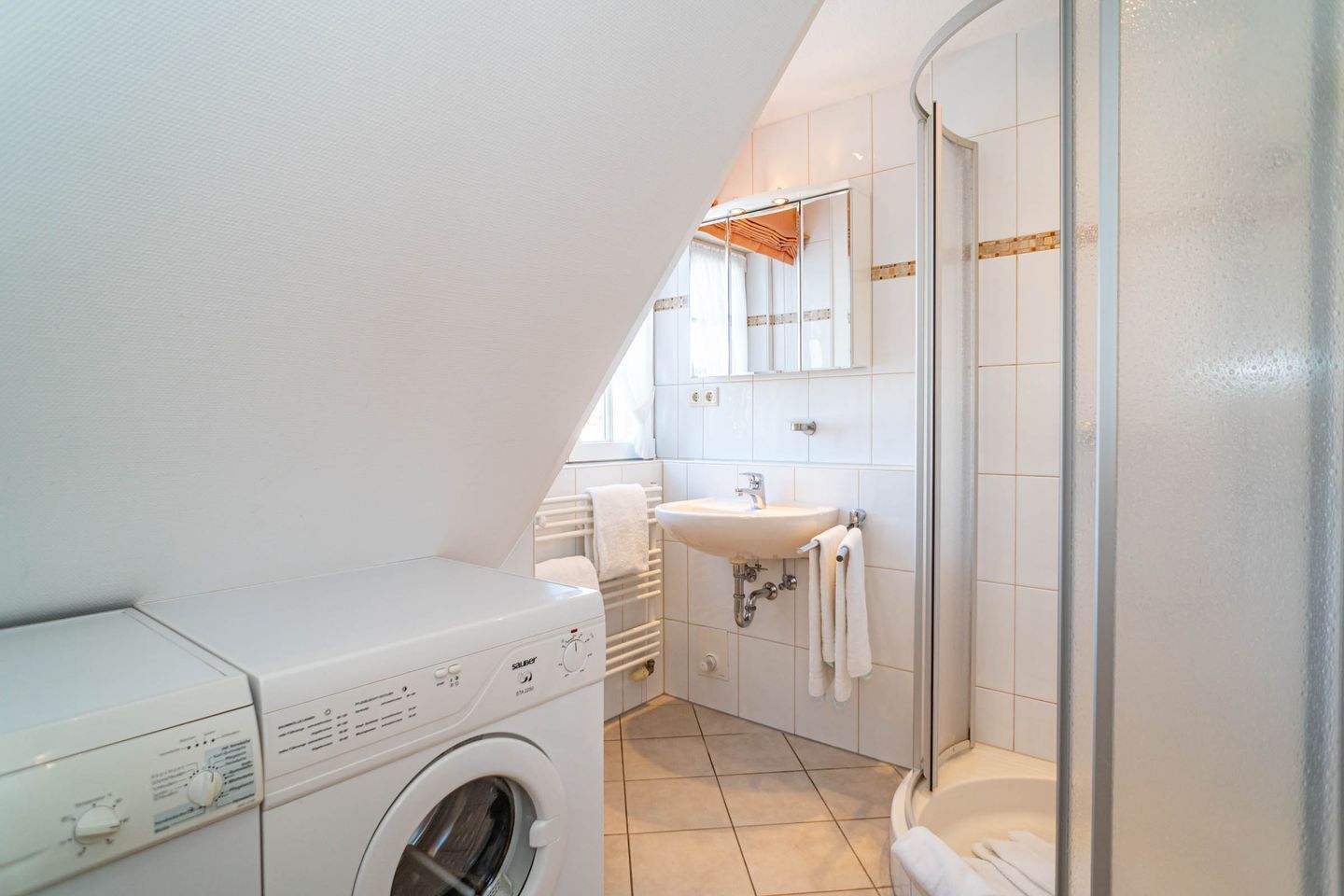 A compact, modern bathroom with a washing machine, a sink, and a shower.