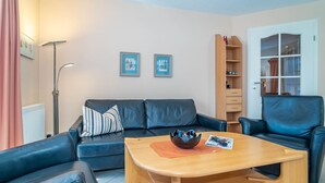 A living room with a black leather sofa, a wooden coffee table, and a bookshelf. - Ammerland Whg. 2 - Spacious 3-room apartment for up to 4 persons, with balcony. (Sylt)